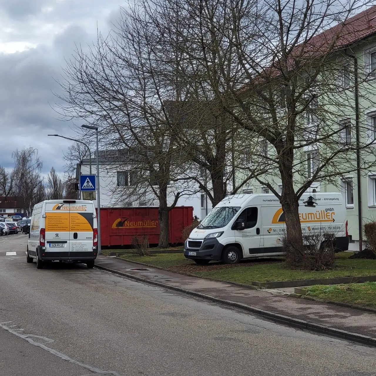 Zwei Transporter und ein Absetzcontainer der Neumüller GmbH an einer Wohnstraße