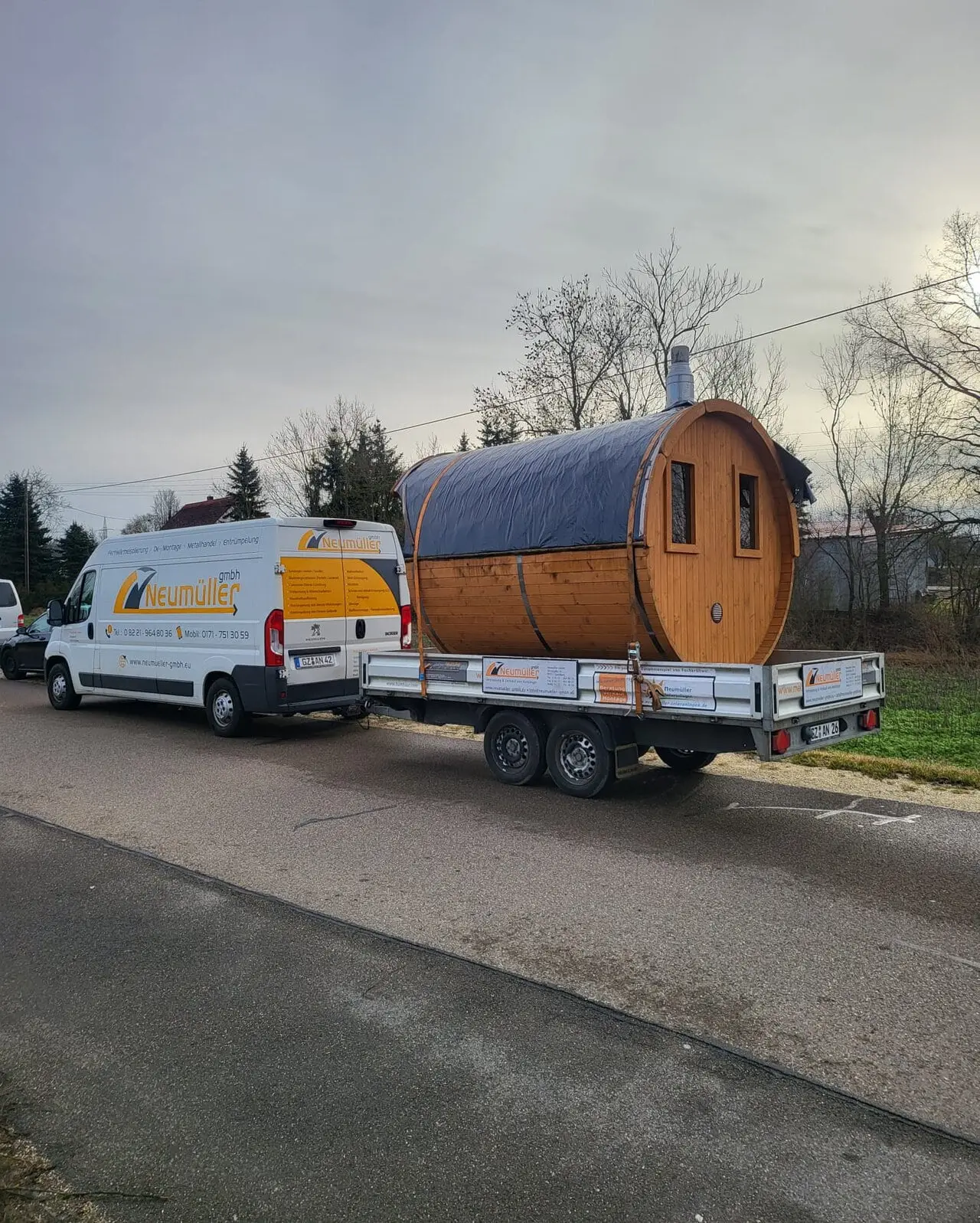 Fahrzeug der Neumüller GmbH mit Tandem-Pritschenanhänger, darauf eine Fasssauna