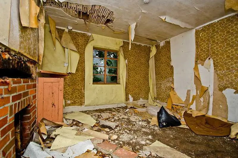 Leerstehender Wohnraum mit gelösten Tapeten und Unrat auf dem Boden vor der Räumung
