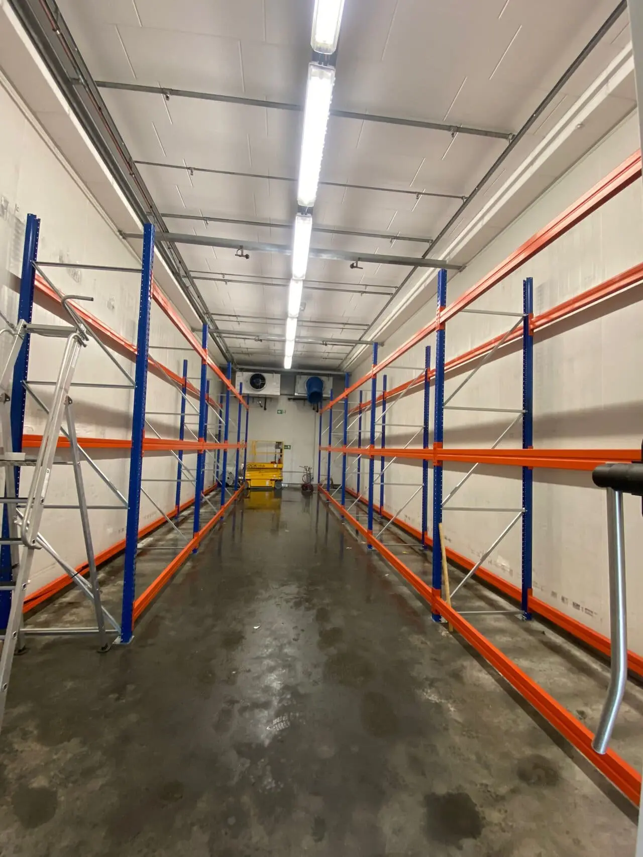 Leergeräumte Lagerhalle mit blau-orangefarbenen Palettenregalen nach der Entrümpelung