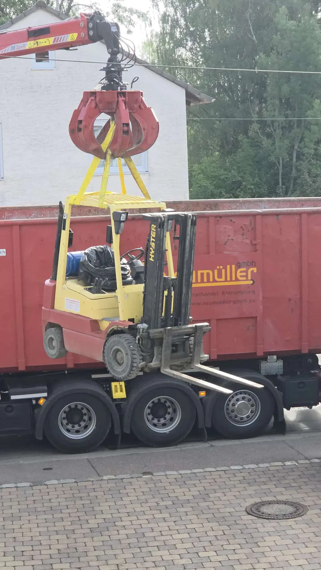 Ladekran der Neumüller GmbH hebt einen Gabelstapler auf einen Abrollcontainer